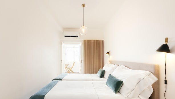 A hotel room with two beds, a bedside table, a lamp, and a window with curtains. - Feel Porto Classic Apartment (Oporto)