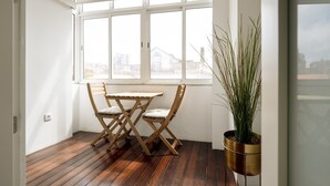 A room with a wooden floor, a table with chairs, a large window, and a potted plant. - Feel Porto Classic Apartment (Oporto)