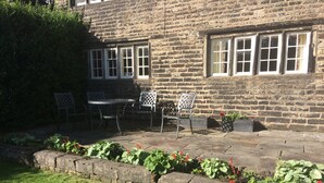 A stone building with a patio area featuring a table and chairs, surrounded by a flower bed. - Hawkyard's Cottage (Oldham)