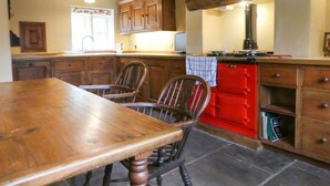 A kitchen with wooden cabinets, a red stove, and a wooden dining table with chairs. - Hawkyard's Cottage (Oldham)