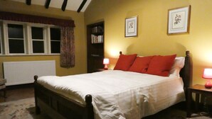 A bedroom with a bed, two bedside lamps, a bookshelf, and a window with curtains. - Hawkyard's Cottage (Oldham)