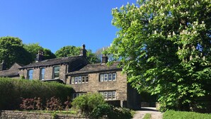 A stone house with a traditional design, featuring multiple windows and a stone wall in front. - Hawkyard's Cottage (Oldham)