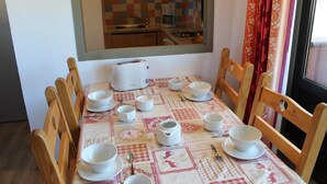 A dining area with a table set for four, surrounded by wooden chairs. A window with a view of a kitchen is above the table. - 50m from ski slopes, 4th floor, balcony, ski locker, 39m², Val Thorens (Val Thorens)
