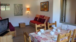A cozy room with a wooden sofa, a TV, a dining table with cups and a toaster, and a painting on the wall. - 50m from ski slopes, 4th floor, balcony, ski locker, 39m², Val Thorens (Val Thorens)