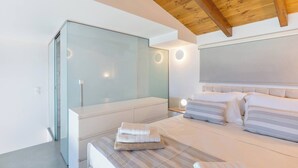 A modern bedroom with a glass shower, a bed with striped bedding, and a wooden ceiling. - OceanEye Suites - Fortuna (Panormo)