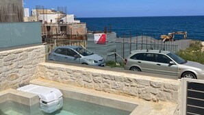 A rooftop pool with a stone wall, a view of the sea, and parked cars. - OceanEye Suites - Fortuna (Panormo)