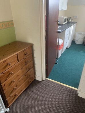 Ein Zimmer mit einem Holzkoffer, einer Küchenzeile mit einer Mikrowelle und einem Mülleimer.