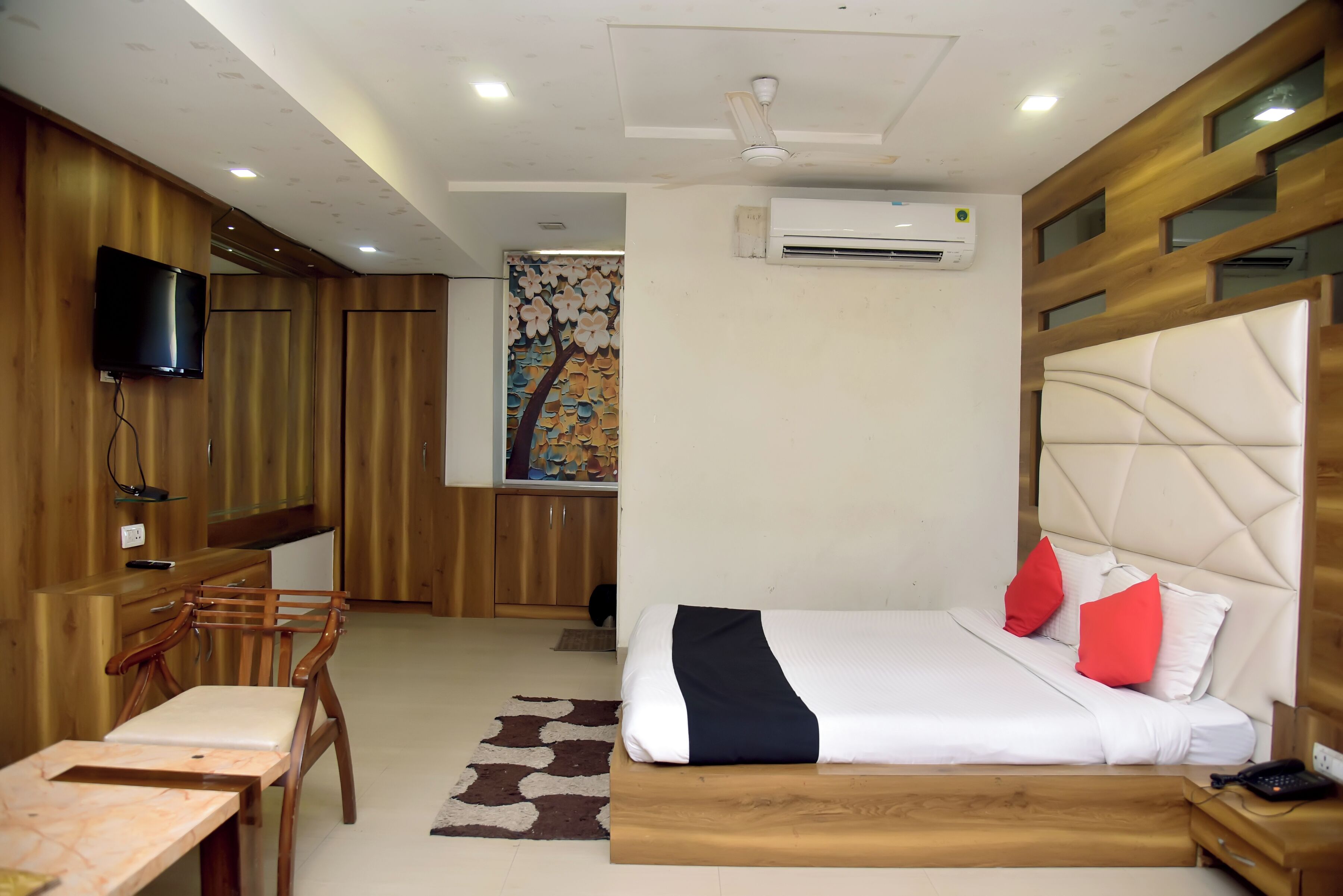 A hotel room with a bed, a desk, a chair, a television, and an air conditioning unit.