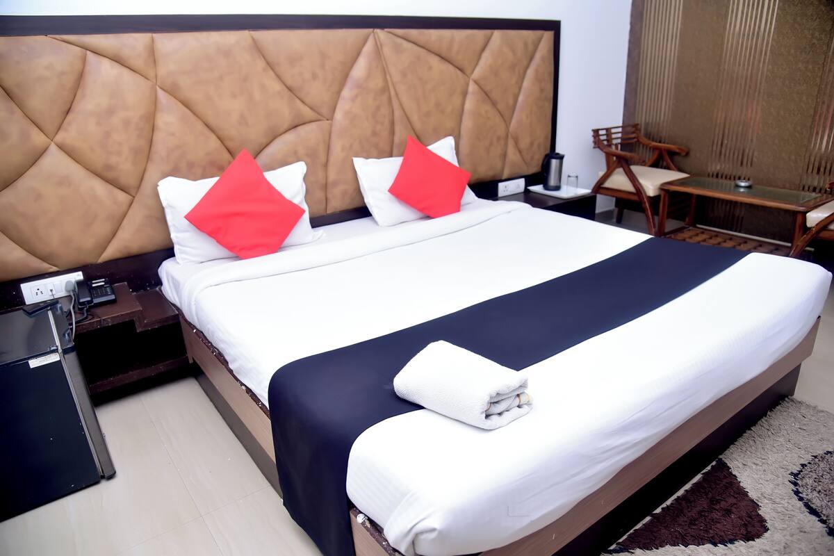 A neatly made bed with a headboard, a bedside table with a phone, and a chair.