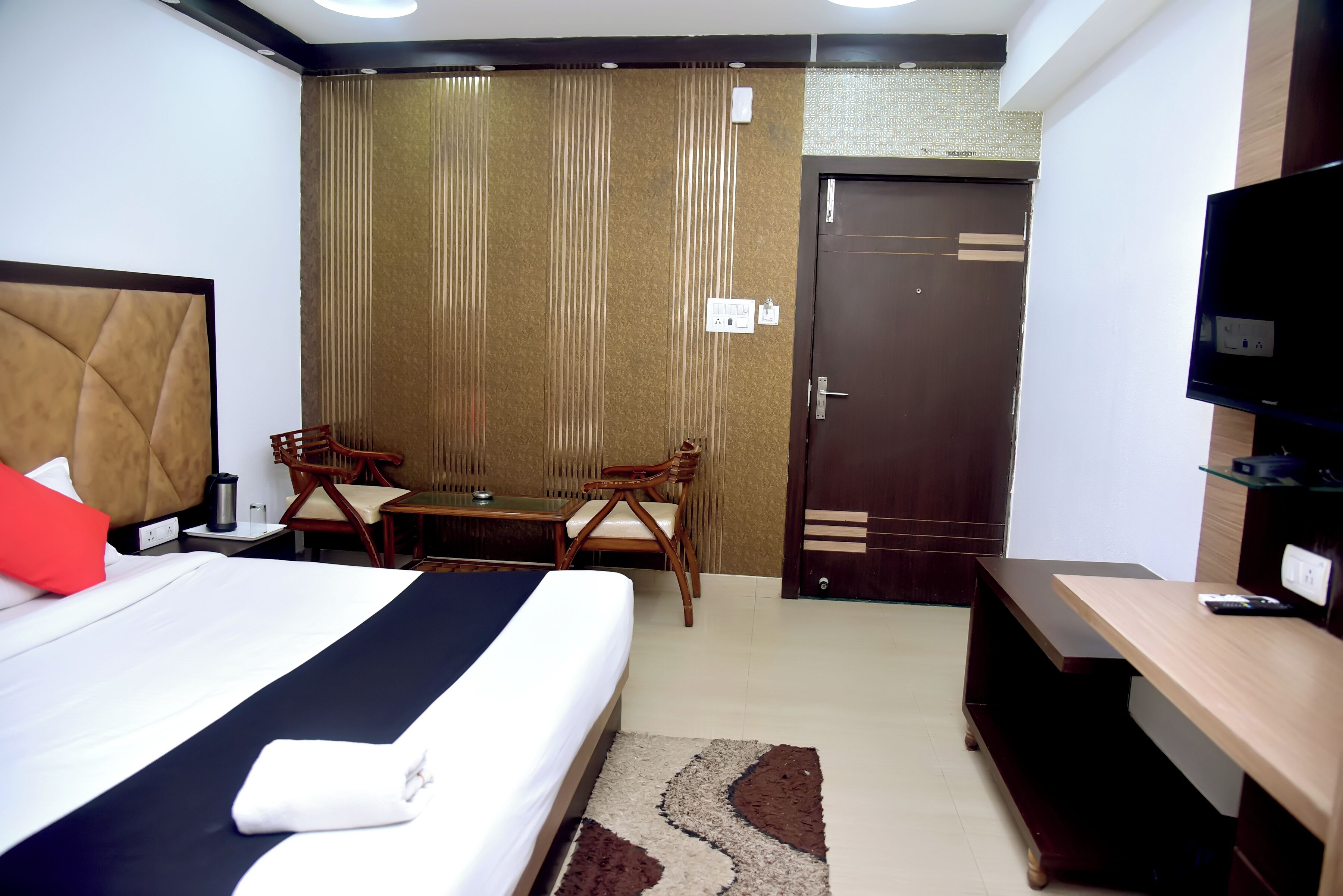 A hotel room with a bed, a desk, two chairs, a television, and a wardrobe.