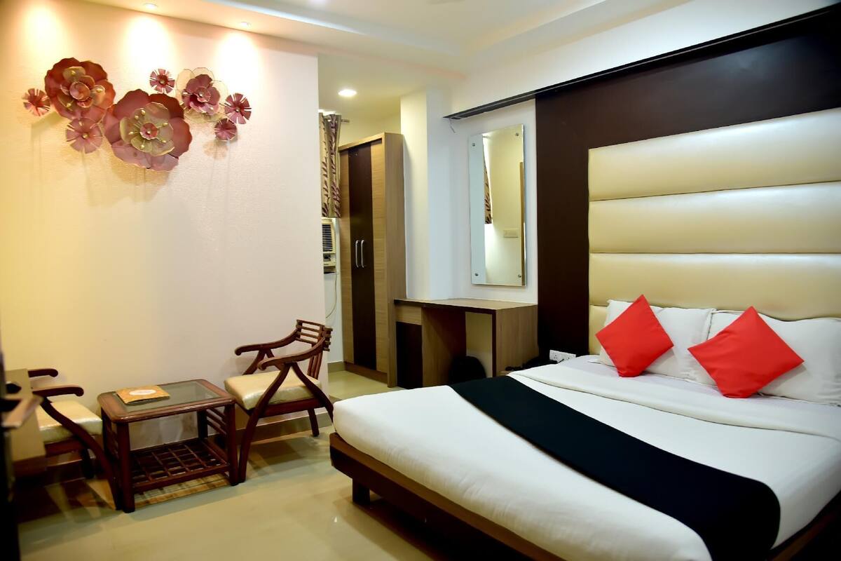 A hotel room with a bed, a small table, two chairs, a mirror, and a wall decoration.