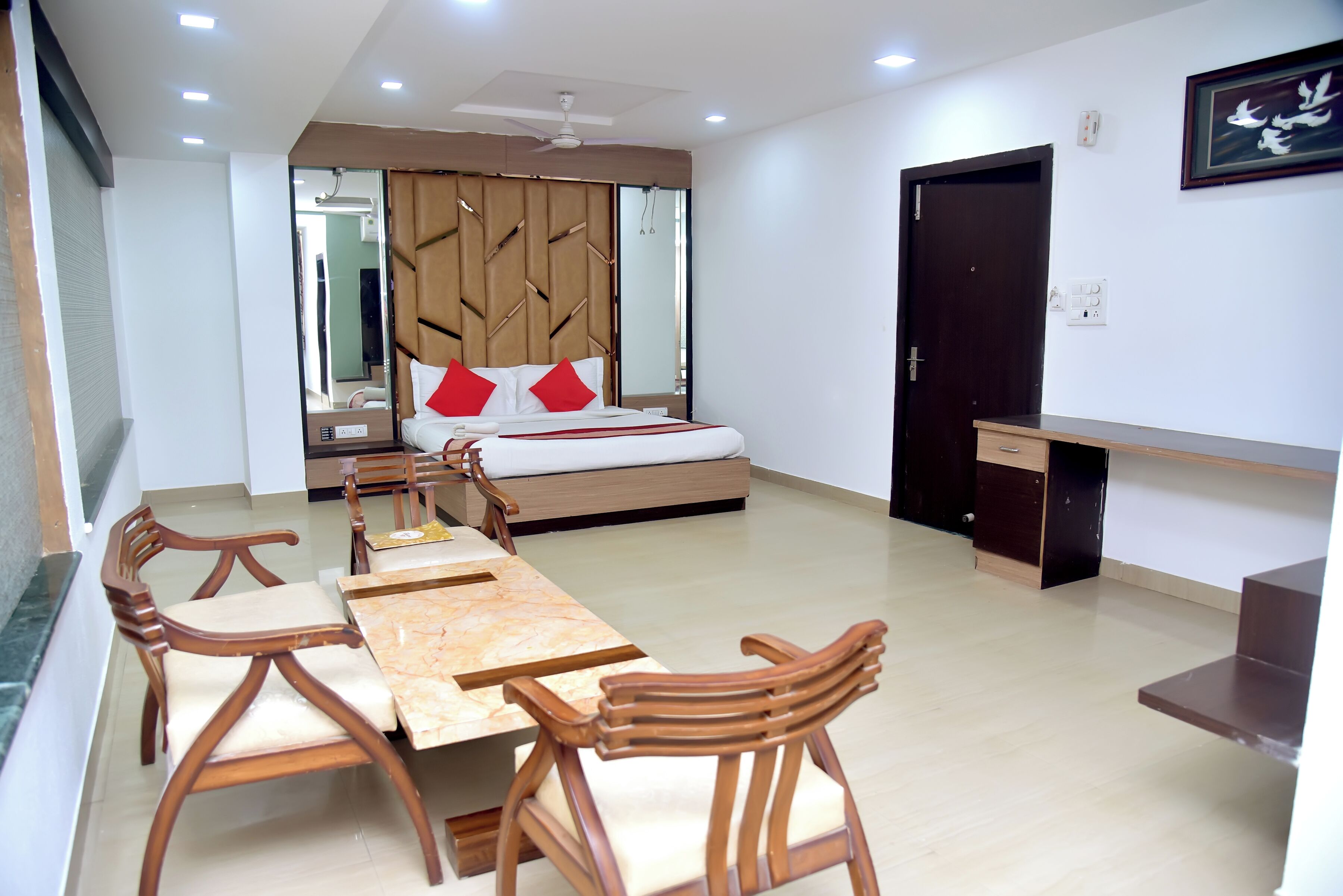 A hotel room with a bed, a desk, a dining table with chairs, and a mirror.