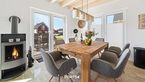 Un comedor moderno con una mesa de madera, sillas tapizadas de gris, una chimenea y vistas al exterior.
