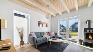 Una sala de estar moderna con un sofá gris, una mesa de centro redonda, una chimenea y un ventanal con persianas.