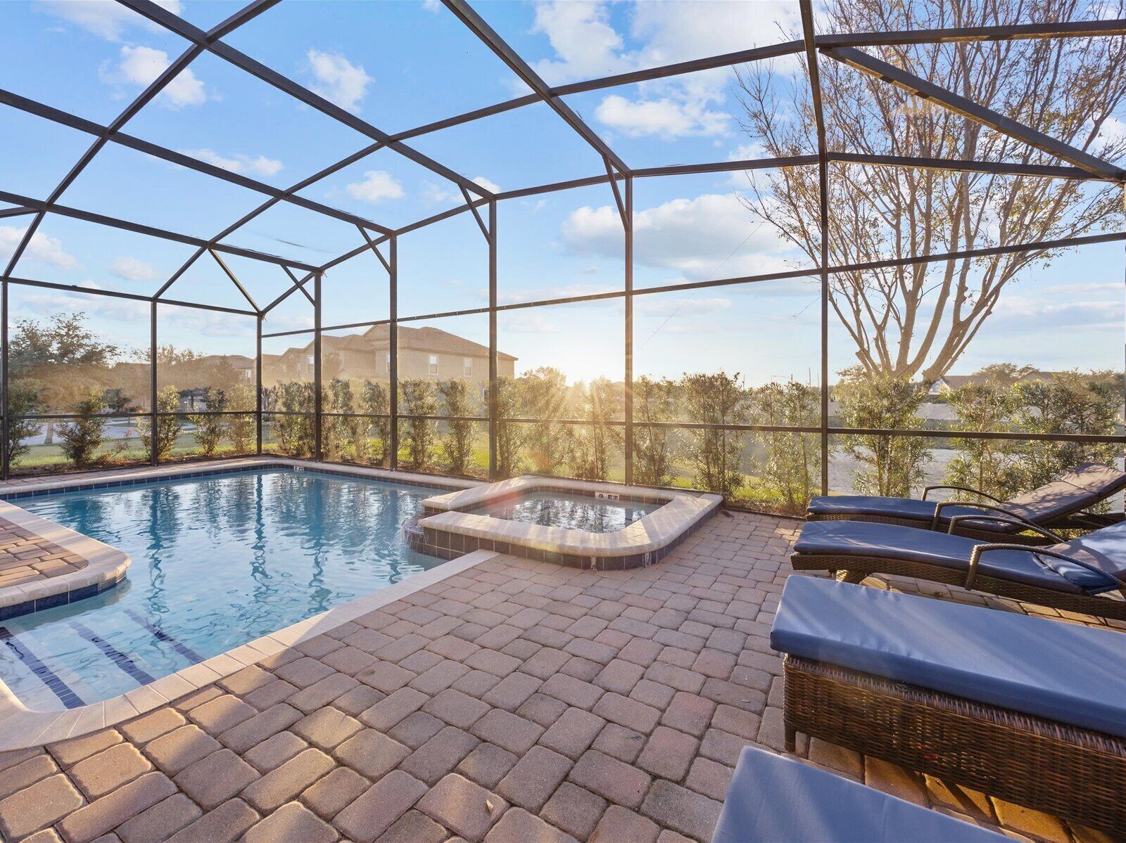 A covered outdoor swimming pool with lounge chairs and a hot tub, surrounded by a metal frame and glass panels.
