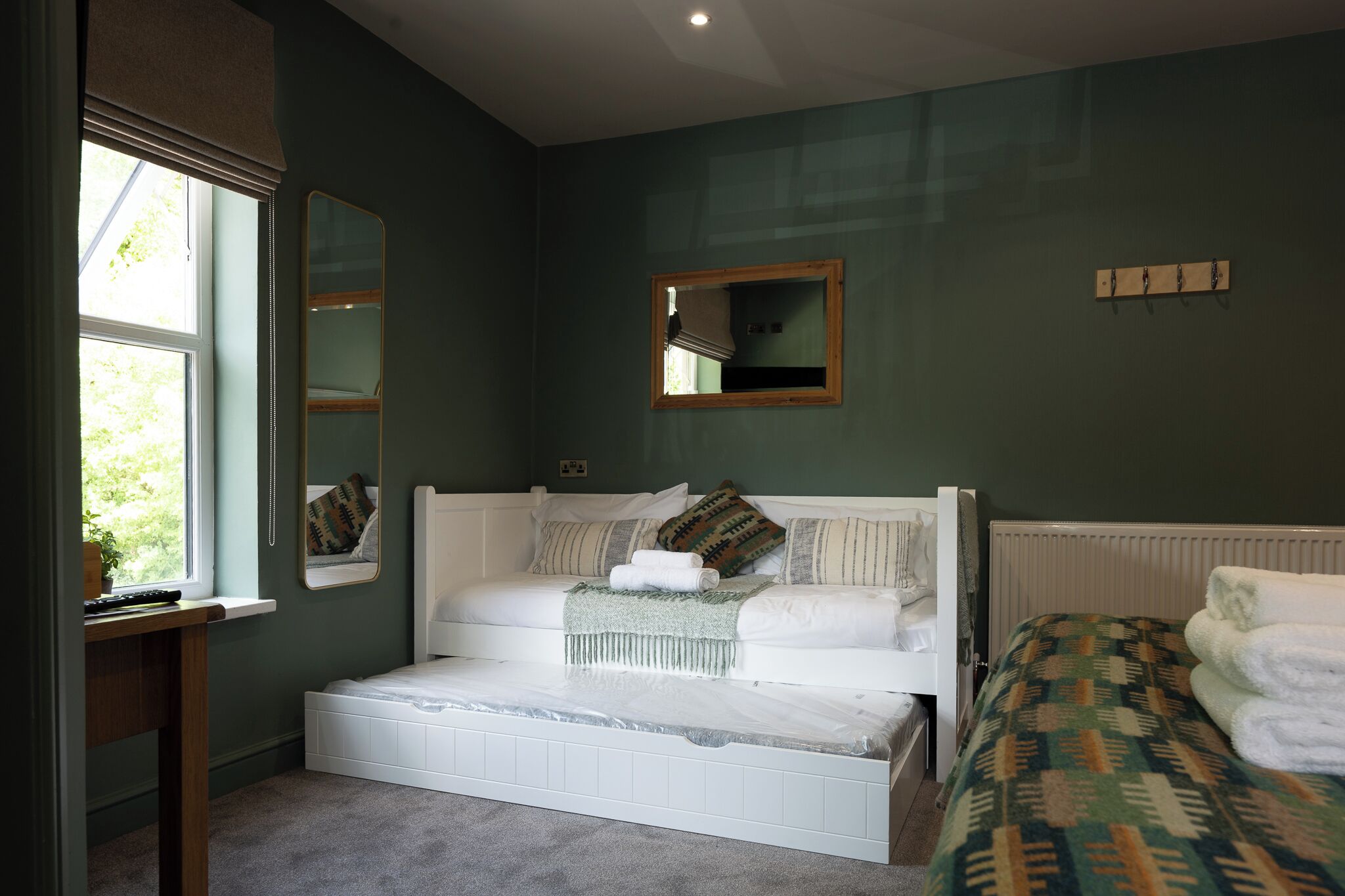Ein Schlafzimmer mit Bett, Nachttisch, Spiegel, Heizkörper und Fenster.