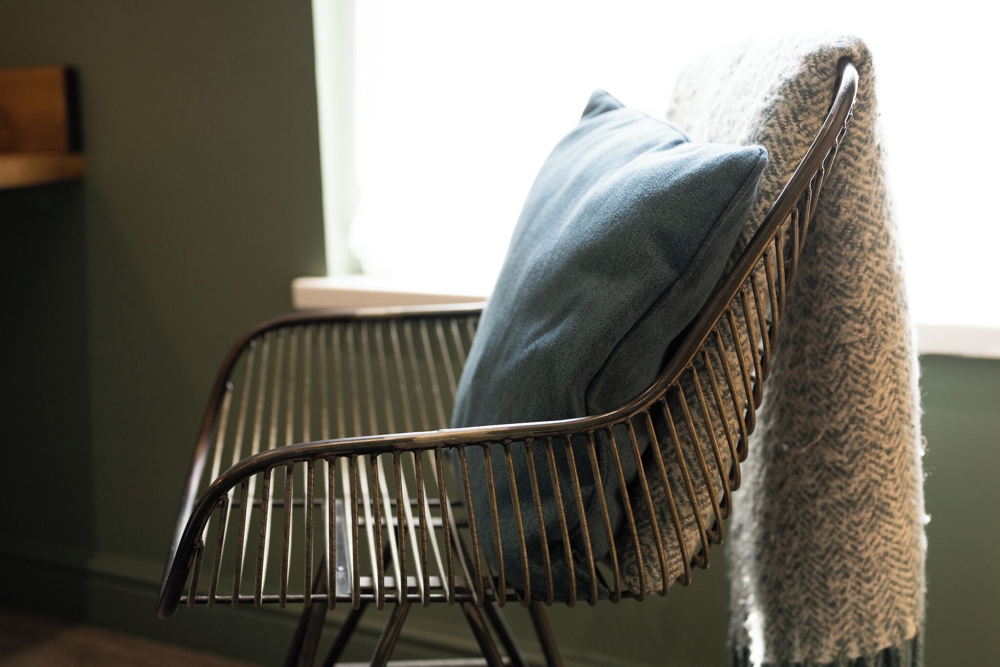 A metal-framed chair with a cushion, a textured blanket, and a window in the background.