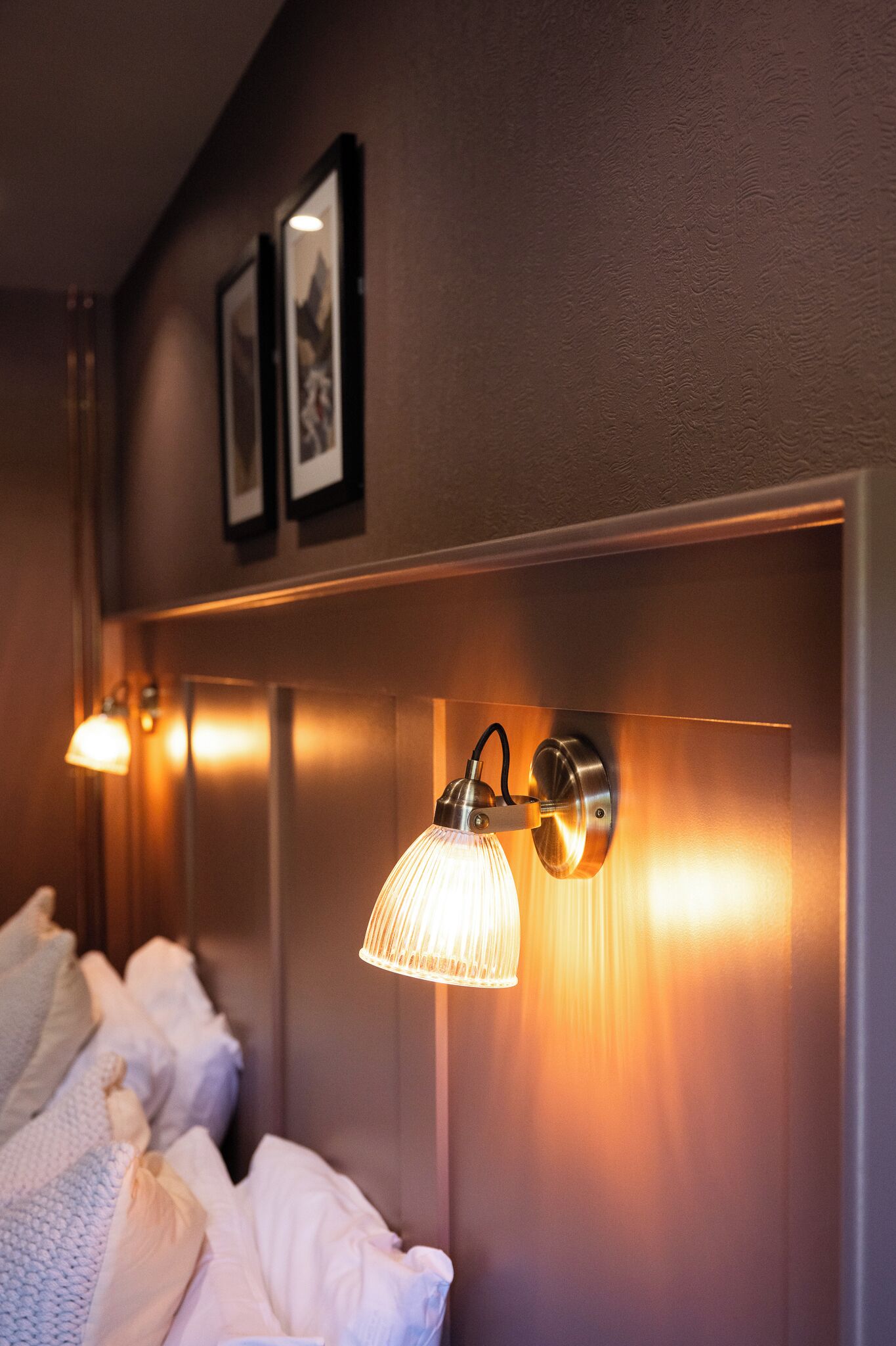 Une chambre d’hôtel avec un lit, un luminaire fixé au mur et des tableaux encadrés au-dessus du lit.