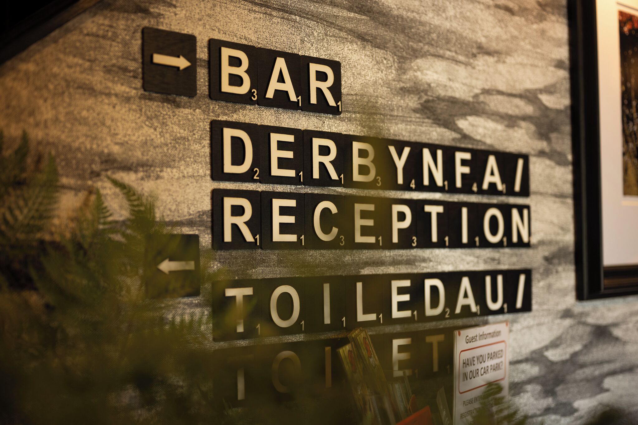 Un muro con segnali direzionali per 'Bar', 'Derbynfa Reception' e 'Toiletau'.