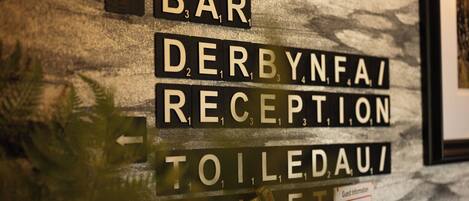 A wall with directional signs for 'Bar', 'Derbynfa Reception', and 'Toiletau'.