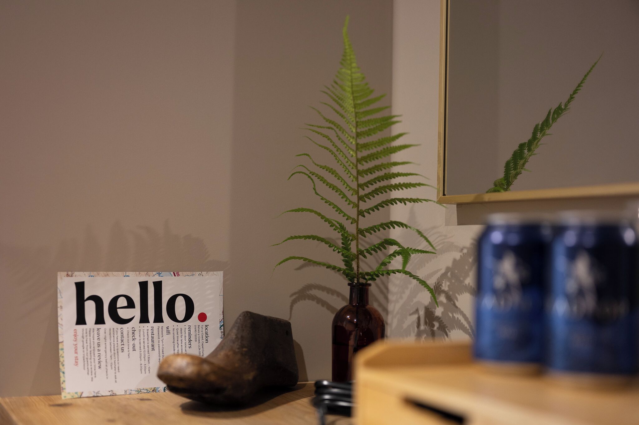 A wooden table with a sign, a plant, a mirror, and a blue mug.