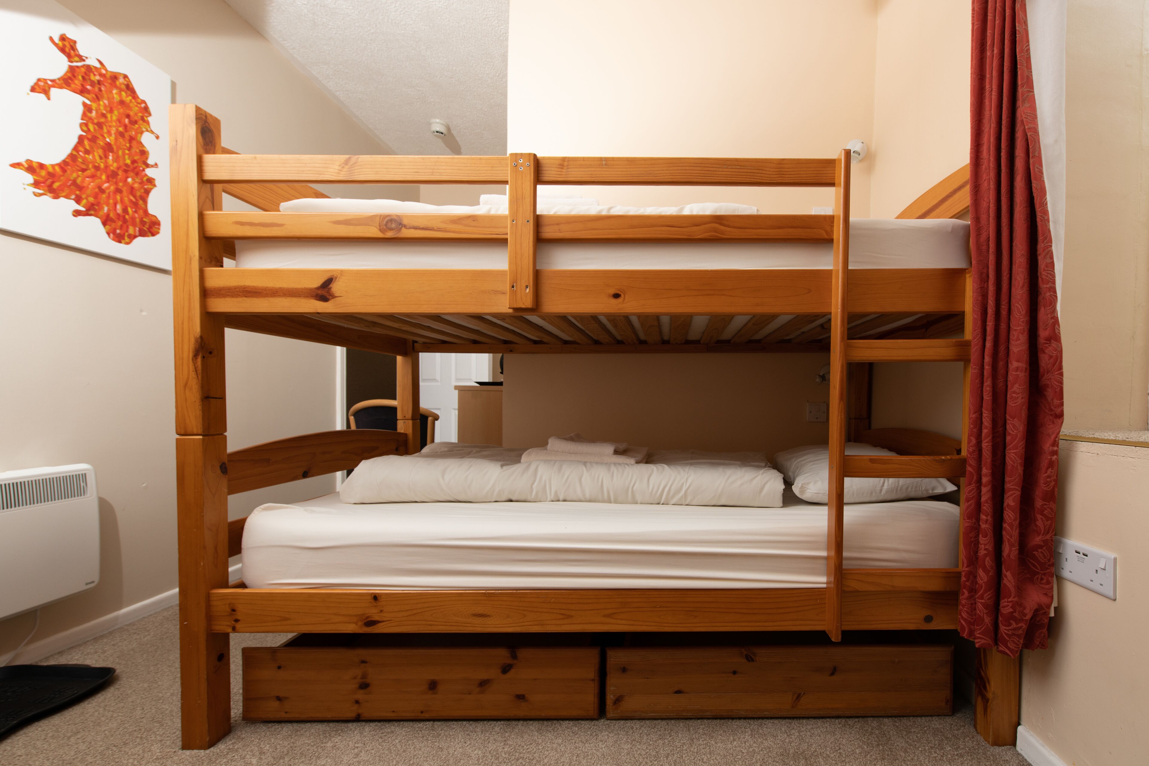 Een stapelbed met houten frame, witte beddengoed en een rood gordijn.