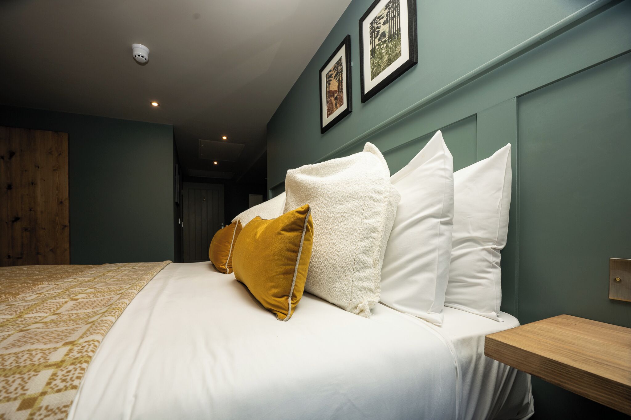 Une chambre d’hôtel avec un lit, une table de chevet en bois et un luminaire fixé au mur.