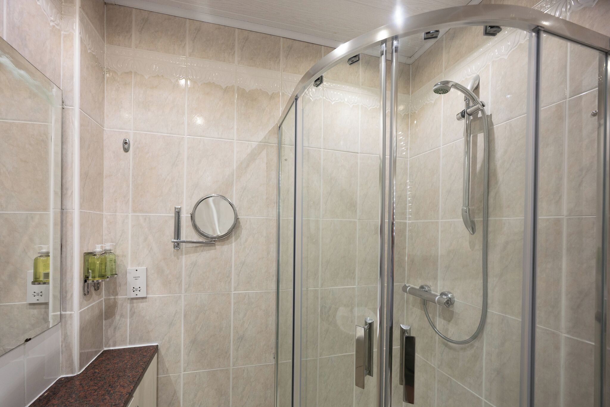 A glass-enclosed shower with a handheld showerhead and a wall-mounted faucet.