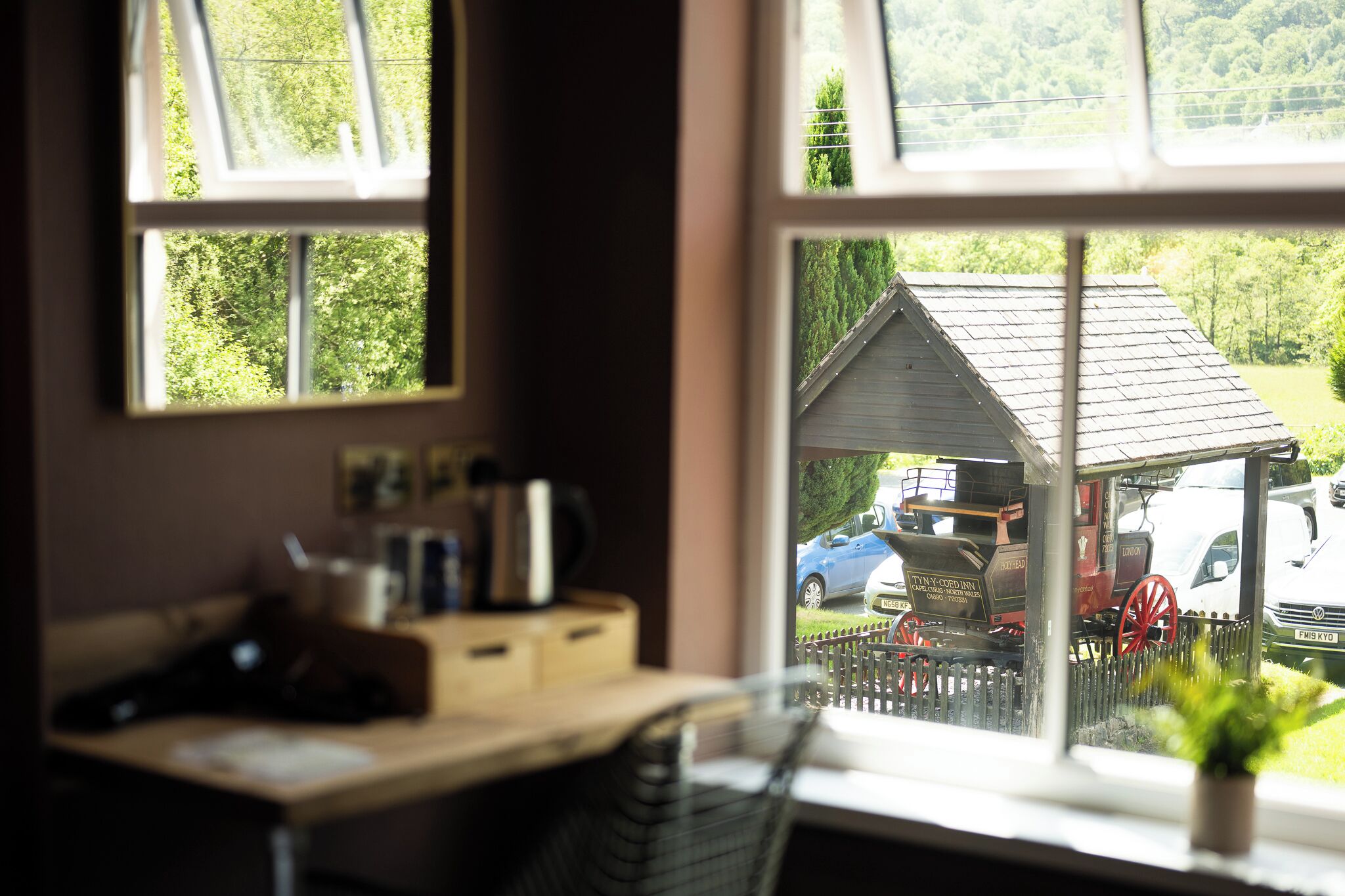 A room with a desk, a chair, a window, and a view of a train and cars outside.