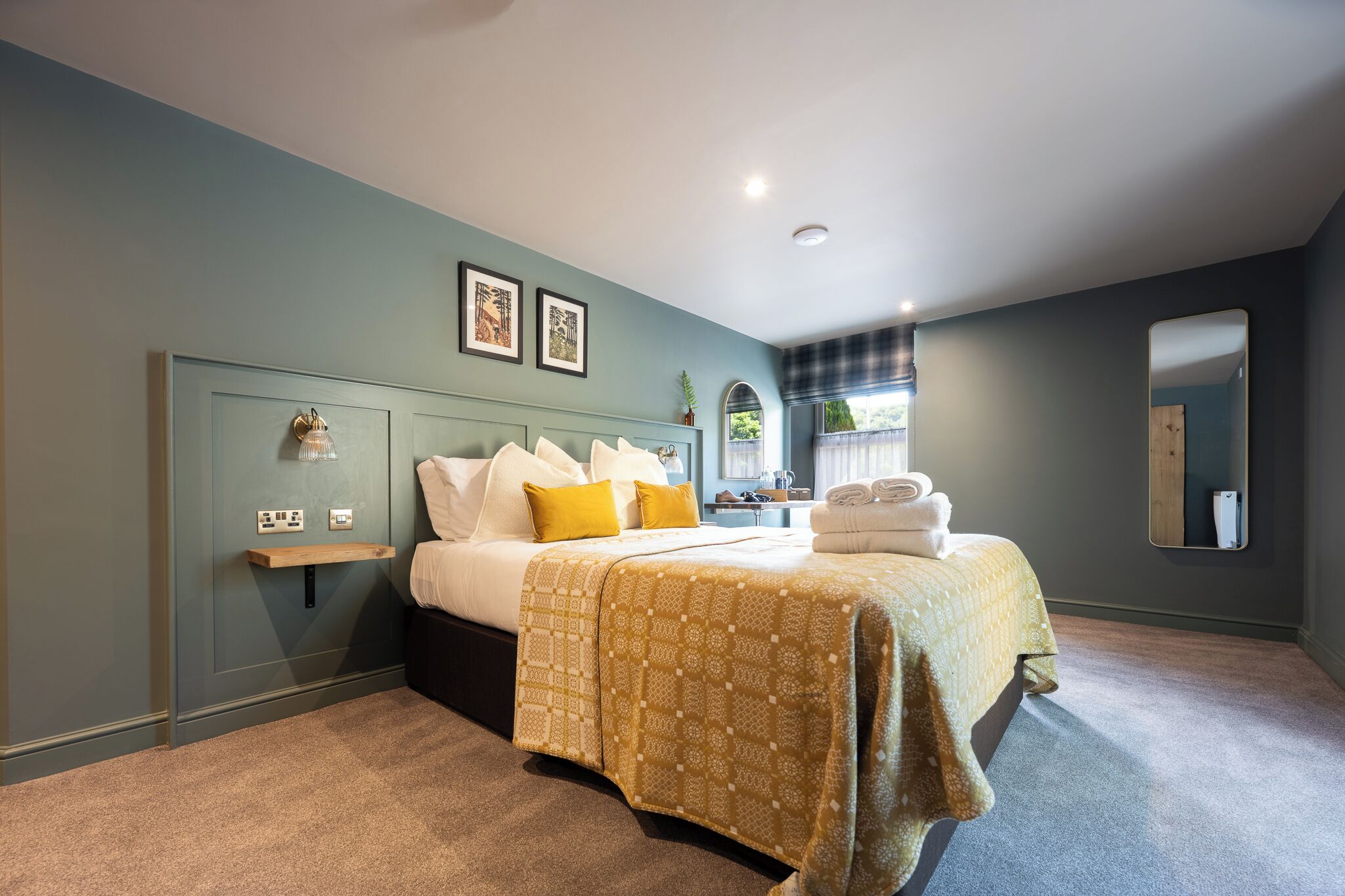 Une chambre à coucher avec un lit, une table de chevet, un miroir et une fenêtre avec des rideaux.