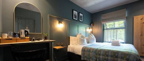 A bedroom with a bed, bedside tables, a desk, a chair, a mirror, and a window with a view.