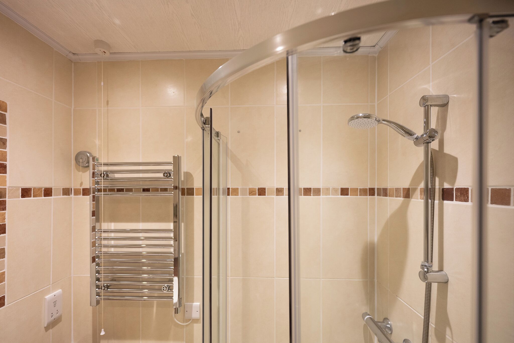 A shower area with a glass door, a handheld showerhead, and a towel rack.