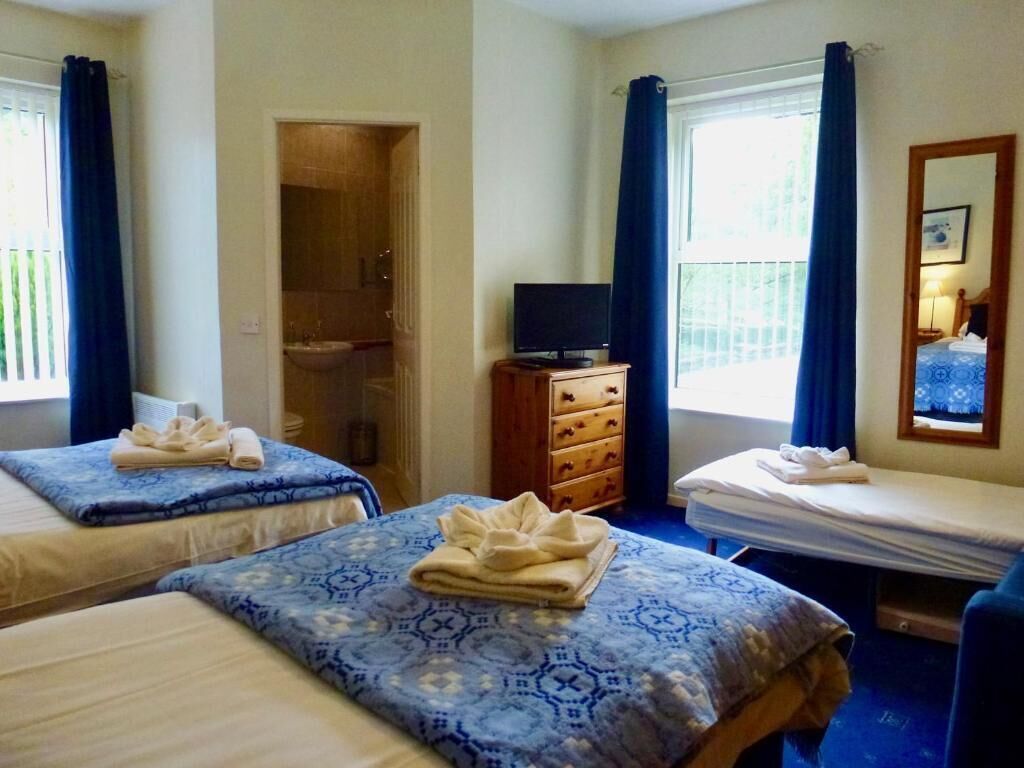 A hotel room with two beds, a television, a dresser, and a window with curtains.