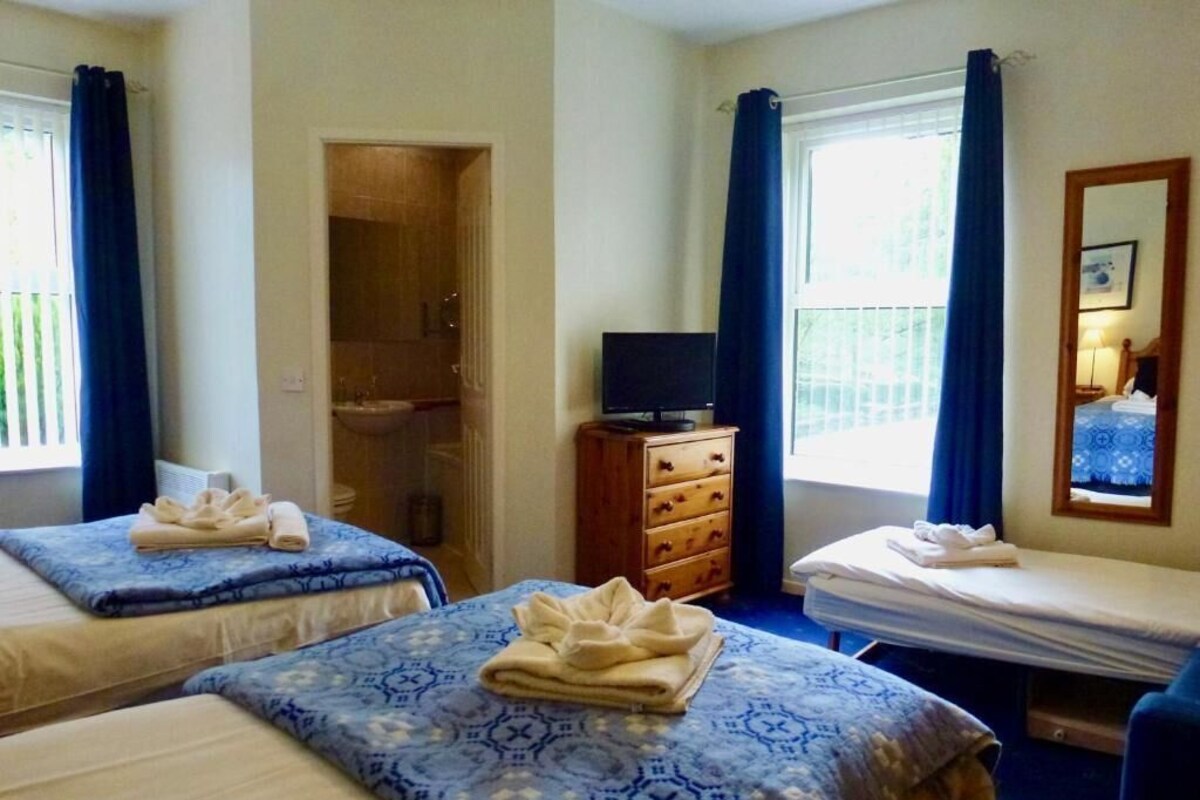 A hotel room with two beds, a television, a dresser, and a window with curtains.