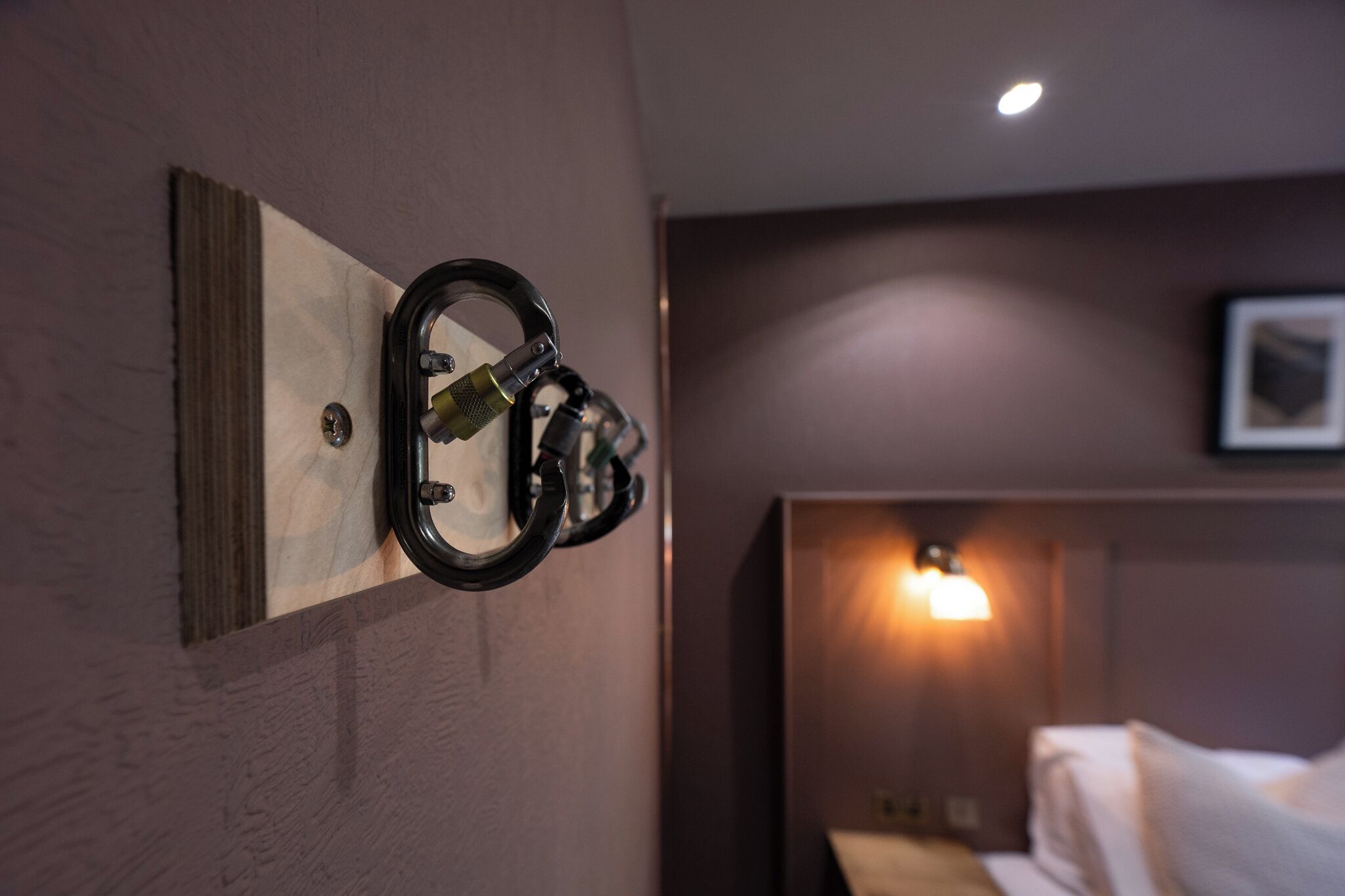 A hotel room with a bed, a wall-mounted coat rack, and a wall-mounted light fixture.