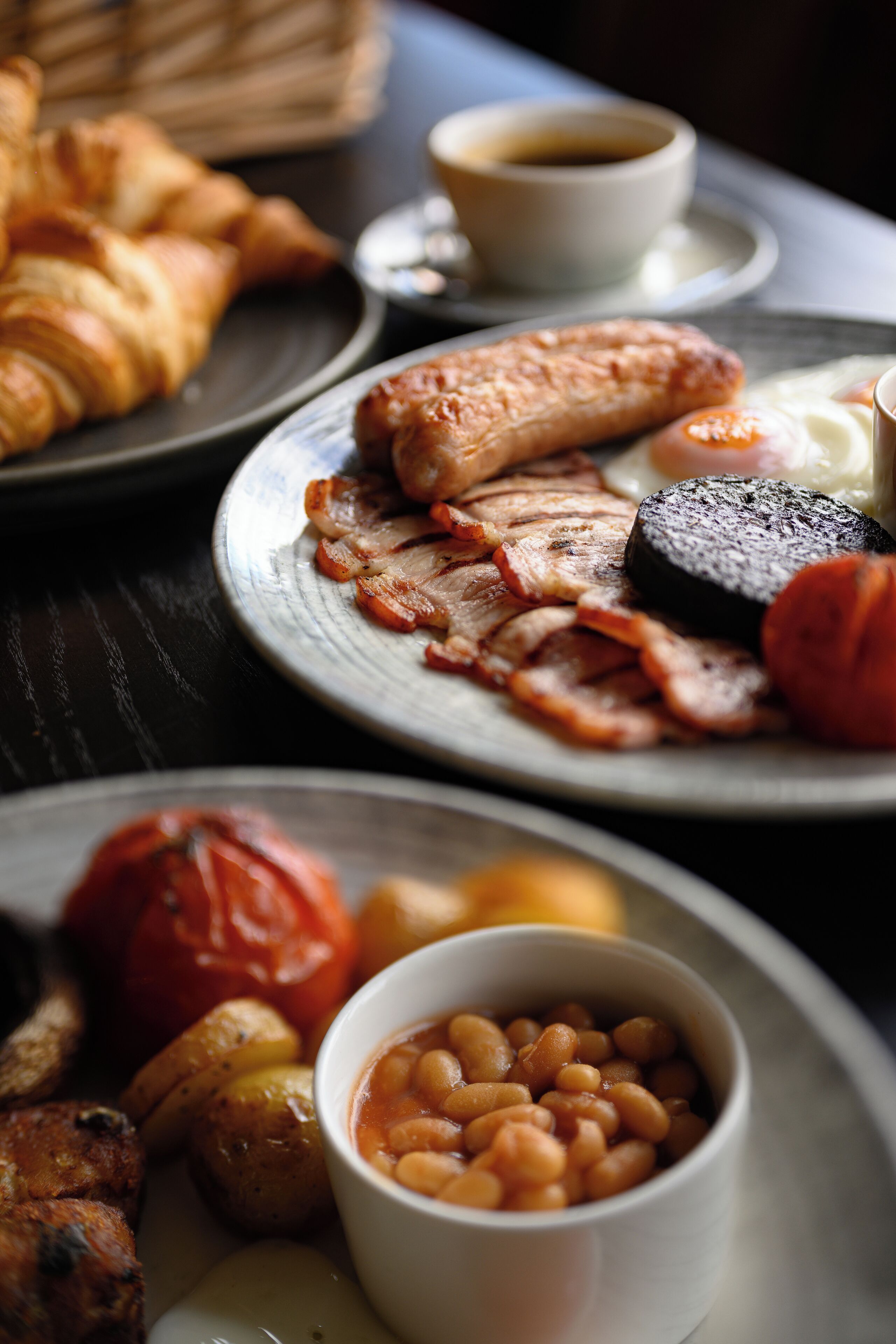 A breakfast setting with plates of food including sausages, bacon, eggs, and toast.