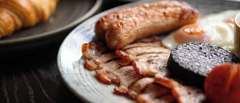 A breakfast setting with plates of food including sausages, bacon, eggs, and toast.