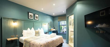 A bedroom with a bed, bedside tables, a mirror, and a TV on the wall.