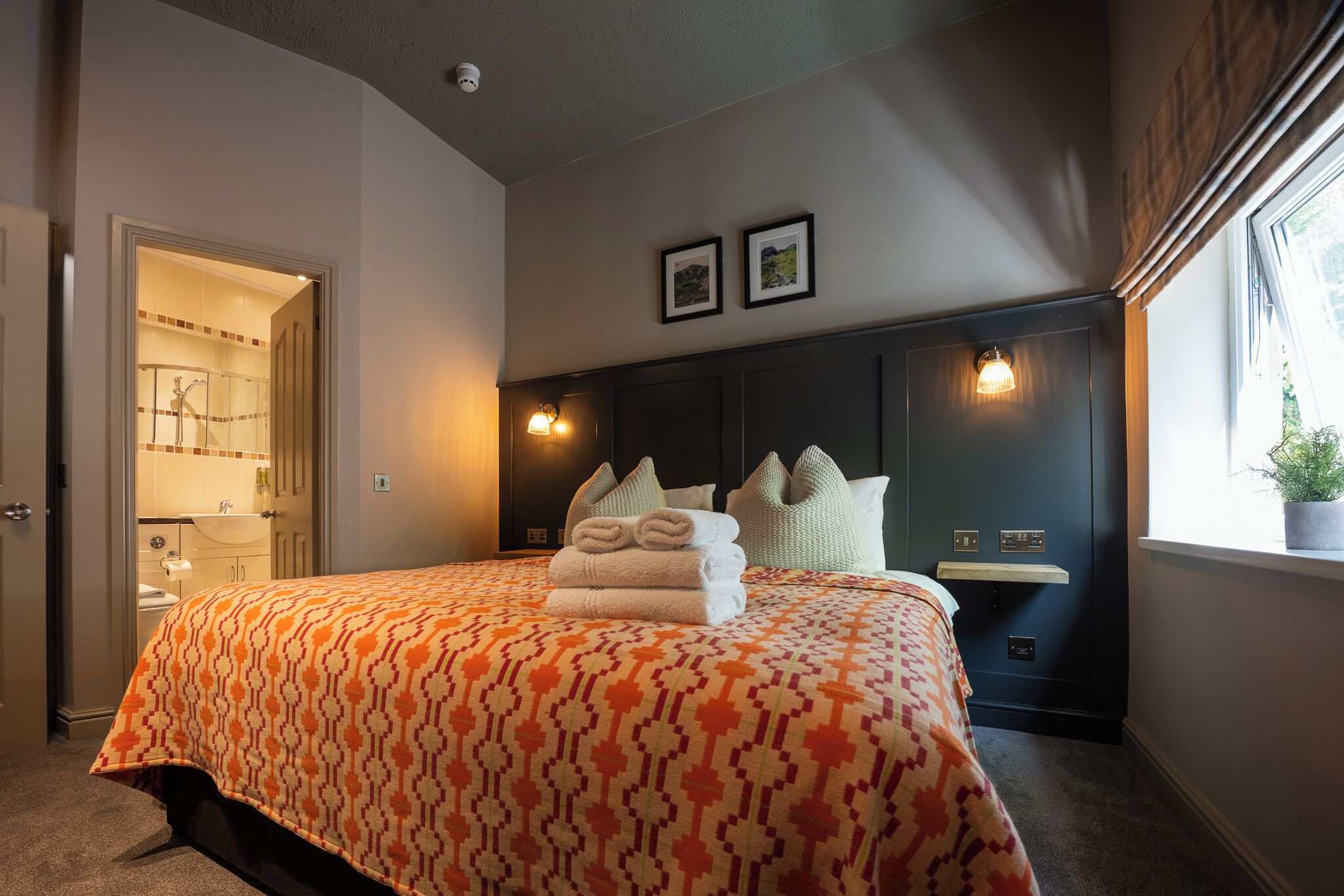 A bedroom with a bed, a nightstand, a window, and a door leading to a bathroom.