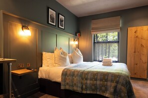 A bedroom with a bed, bedside table, wall-mounted lights, a window with a view, and a wooden door. - Tyn-y-Coed Hotel (Betws-Y-Coed)