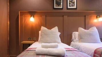 A hotel room with two beds, a nightstand, and wall-mounted lamps.