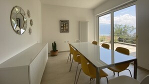A modern dining area with a large table and yellow chairs, a potted cactus, and a view through large windows. - Casa Lara in Menaggio, with pool and beautiful lake view! (Menaggio)