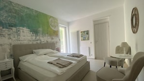 A modern bedroom with a large bed, a chair, a small table, and a painting on the wall. - Casa Lara in Menaggio, with pool and beautiful lake view! (Menaggio)