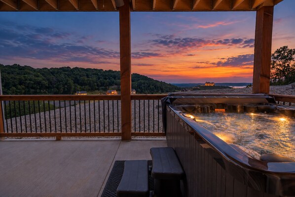 A hot tub under a wooden pergola with a view of a sunset over a forested landscape.