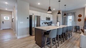 A modern kitchen with white cabinets, stainless steel appliances, and a central island with bar stools. - Hot Tub, Lake Views, Mins to SDC, Pools-Sleeps 16 (Branson)