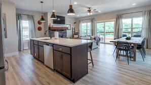 A spacious kitchen with a central island, wooden flooring, pendant lighting, and a dining area with a wooden table and chairs. - Hot Tub, Lake Views, Mins to SDC, Pools-Sleeps 16 (Branson)