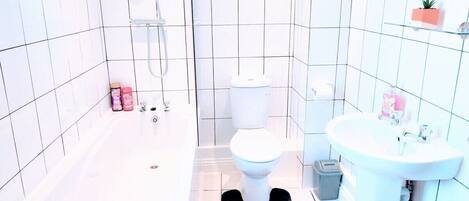A modern bathroom with white tiles, a bathtub, a toilet, and a sink.