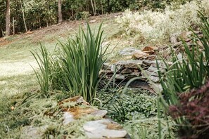 Un jardín con pared de piedra, diversas plantas y un área cubierta de césped.