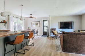 A modern kitchen with a bar area, dining space, and a living area with a sofa and TV. - Hillside Haven: Modern Retreat, Mountain Views (Faber)