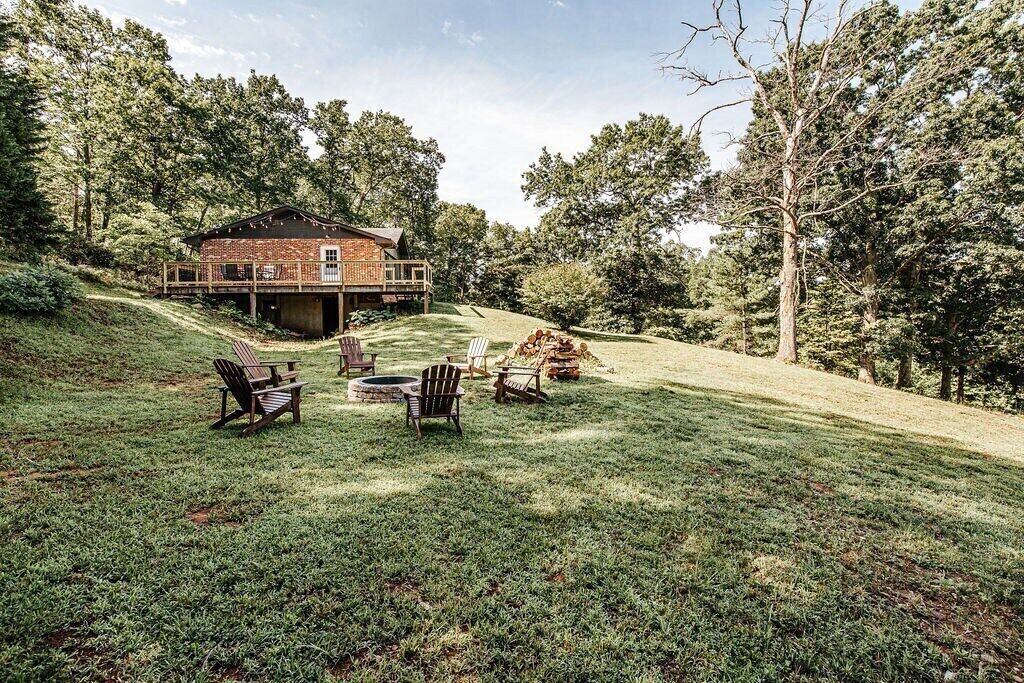 A rustic cabin with a deck, surrounded by a grassy yard and trees.